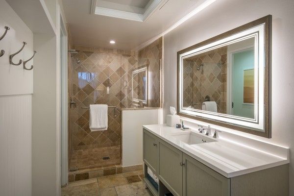 A modern bathroom features a large vanity with twin sinks, a mirror with LED lights, and a spacious walk-in shower with a towel rack.