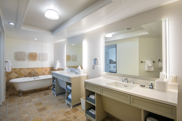 A bathroom with a freestanding bathtub, double sinks, large mirrors, and modern fixtures, featuring tiled floors and walls.