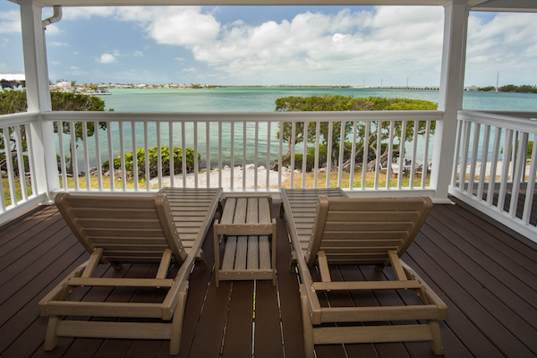 Two lounge chairs on a wooden deck overlook a scenic view of calm waters and a partly cloudy sky, framed by a white railing.