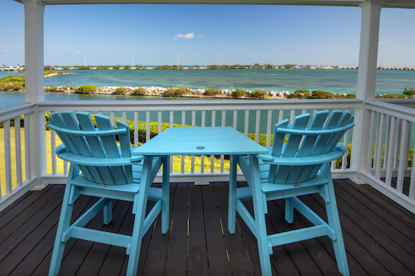 Two blue chairs and a table on a deck overlooking a scenic water view with clear skies.