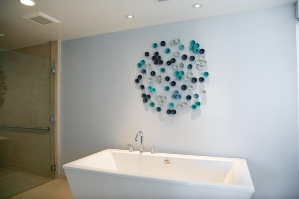 The image shows a modern bathroom with a freestanding bathtub and a decorative wall piece composed of variously colored circular elements.