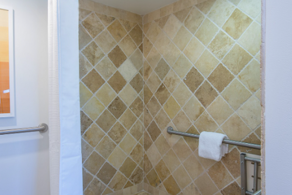 The image shows a tiled, walk-in shower with a curved shower curtain rod and safety grab bars. A towel is on the bar.