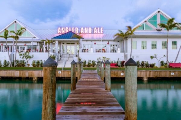 A wooden dock leads to a building with a neon sign reading 