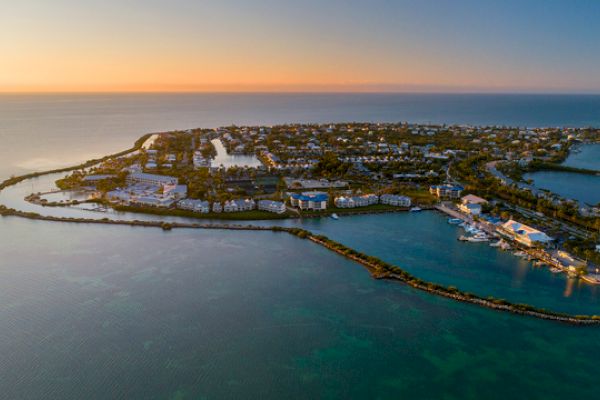 An aerial view of a coastal town with buildings, roads, and surrounding water, taken at sunset, highlighting the serene and scenic landscape.