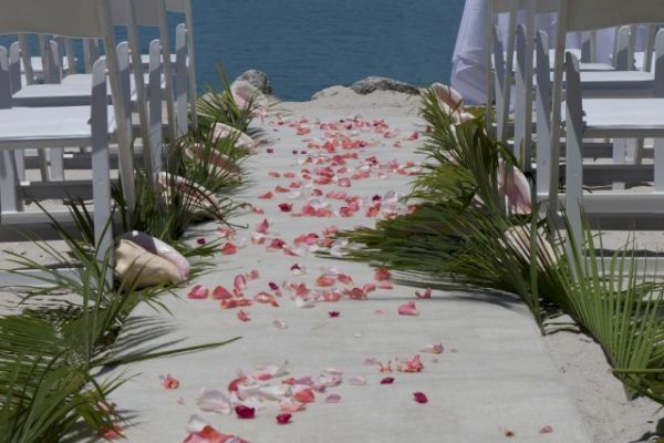 An outdoor wedding setup with white chairs, a flower petal-strewn aisle, and a view of the water in the background.