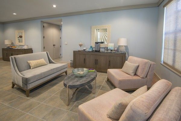 A modern living room with a grey sofa, two beige chairs, and a round coffee table, featuring a sideboard with decorations and soft lighting.