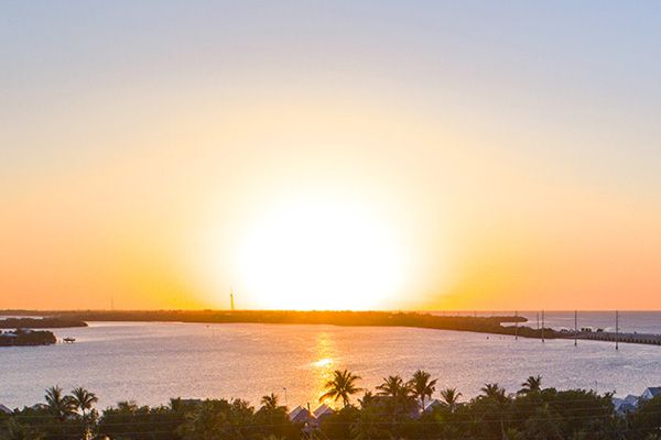 A serene sunset over a body of water with palm trees and buildings in the foreground, creating a peaceful and picturesque scene.