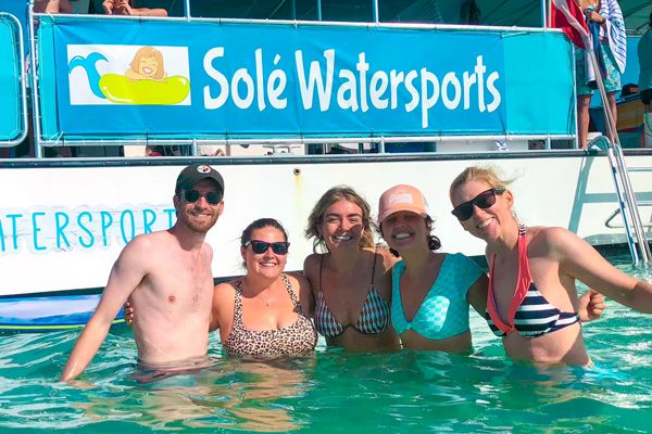 Five people smiling in a body of water in front of a sign that reads 