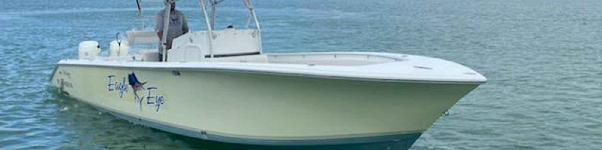 A white fishing boat named "Eagle Eye" is floating on calm waters with lush green trees in the background and a person on board.