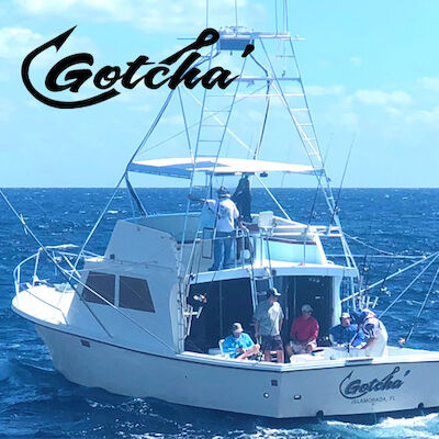 A fishing boat named "Gotcha" with several people on board is on the ocean, featuring a logo above the boat.