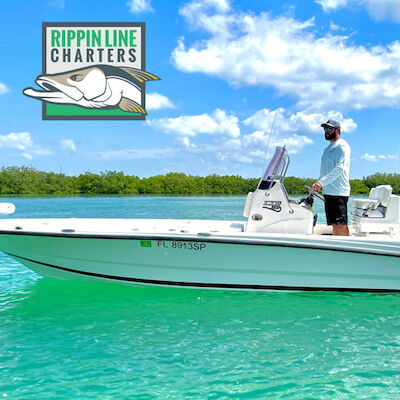 A person stands on a white boat on clear turquoise water with "RIPPIN LINE CHARTERS" logo above. There are green trees and a blue sky in the background.