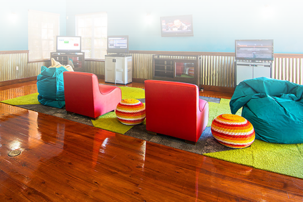 A cozy game room with red chairs, bean bags, multiple screens, and a bright floor, creating a vibrant and inviting atmosphere for entertainment.