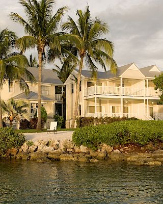 A picturesque waterfront building with palm trees, lush greenery, and serene water in the foreground, creating a tranquil tropical atmosphere.