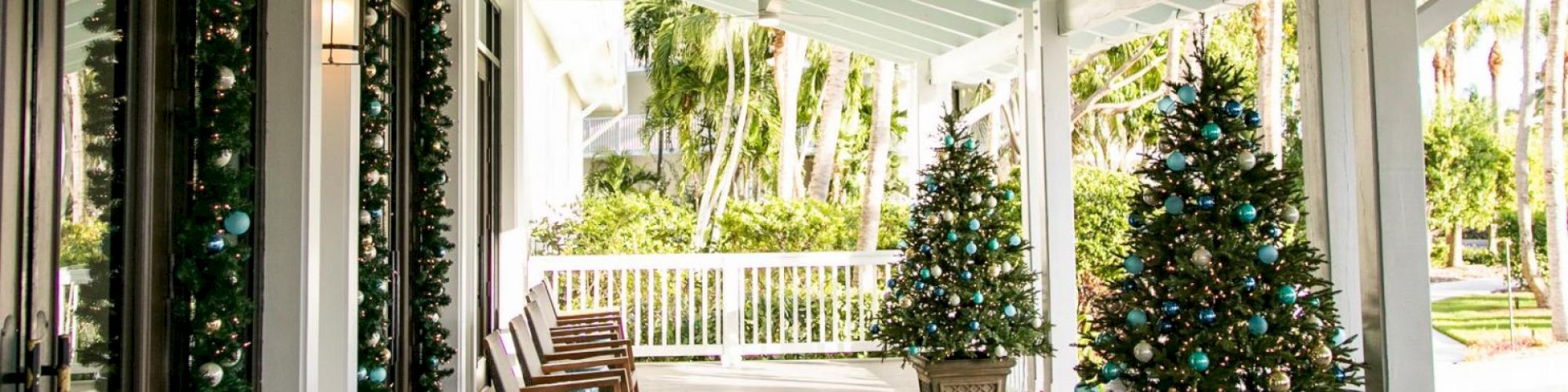 A festive porch with Christmas trees, rocking chairs, and garlands, creating a warm, holiday atmosphere.