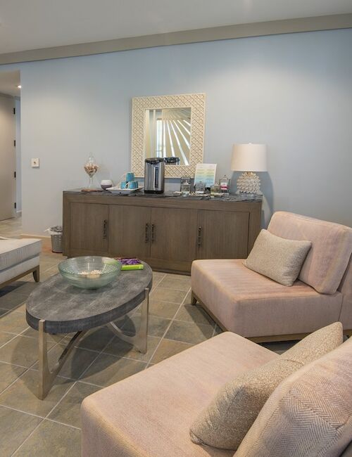 A modern living room with two armchairs, a sofa, and a round coffee table. The room includes a sideboard, lamps, and a painting on the walls.