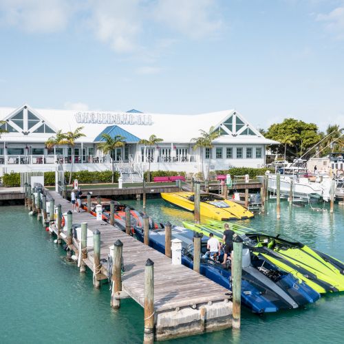 A waterfront area with a marina, colorful boats docked, and a building named "Marina Village" in the background amidst a clear sky.