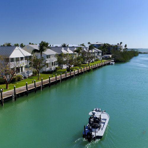 A tranquil canal with houses lined up on the left, lush greenery, and a small boat sailing through the water, under a clear blue sky.