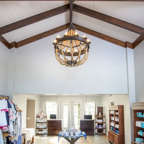 The image shows a well-lit interior space with high ceilings, a chandelier, shelves of merchandise, and a round table displaying items in the center.