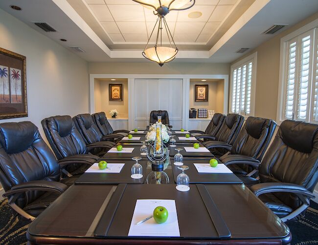 This image depicts a modern conference room with a long table, leather chairs, notepads with green apples, and a decorative chandelier.