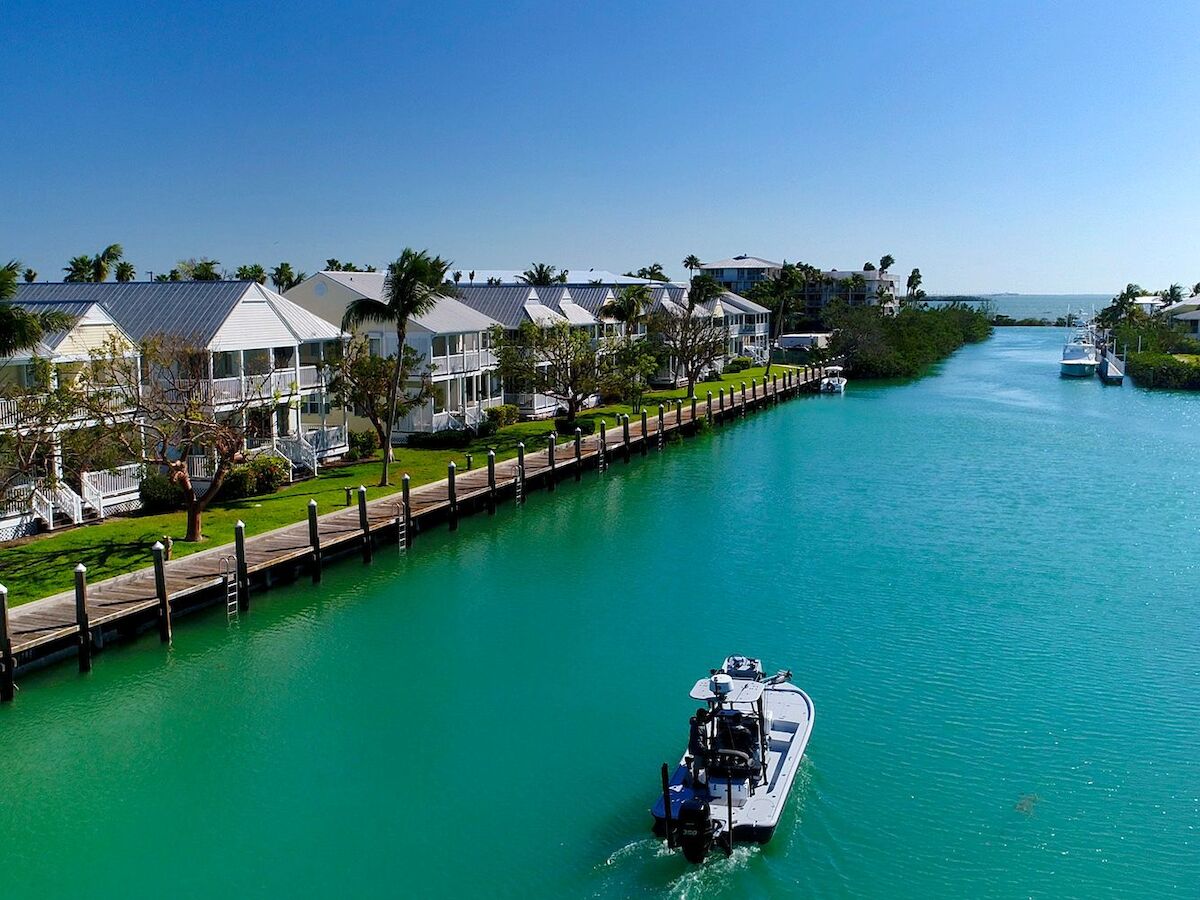 A scenic canal with turquoise water is lined with houses and boats, including one prominently in the foreground, under a clear blue sky.