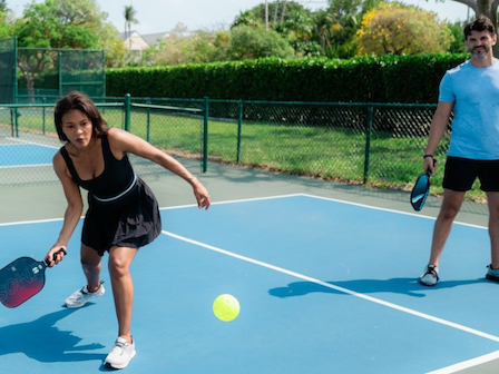 Two people are playing pickleball on an outdoor court, with one ready to hit the ball and the other observing.