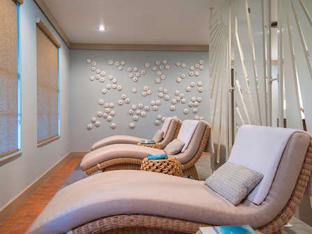 The image shows a tranquil room with three reclining lounge chairs, cushions, soft lighting, and wall art featuring clusters of circular designs.