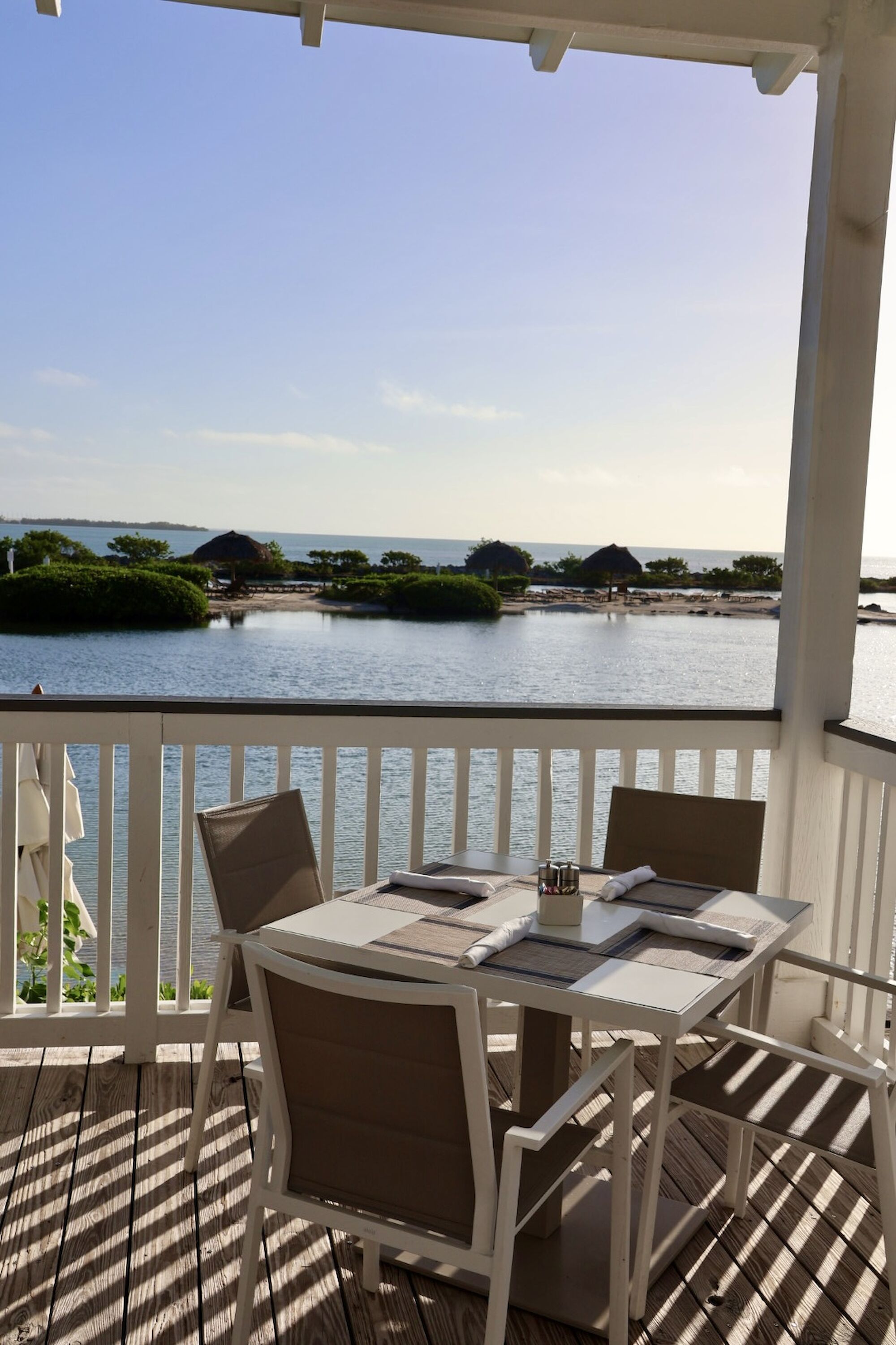 A patio with a table and chairs overlooks a scenic view of water and greenery under a clear sky.