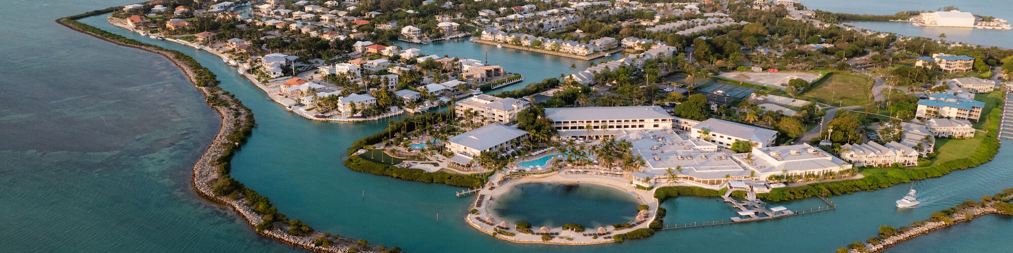 The image shows an aerial view of an island with buildings, surrounded by clear blue water and connected by bridges or roads.