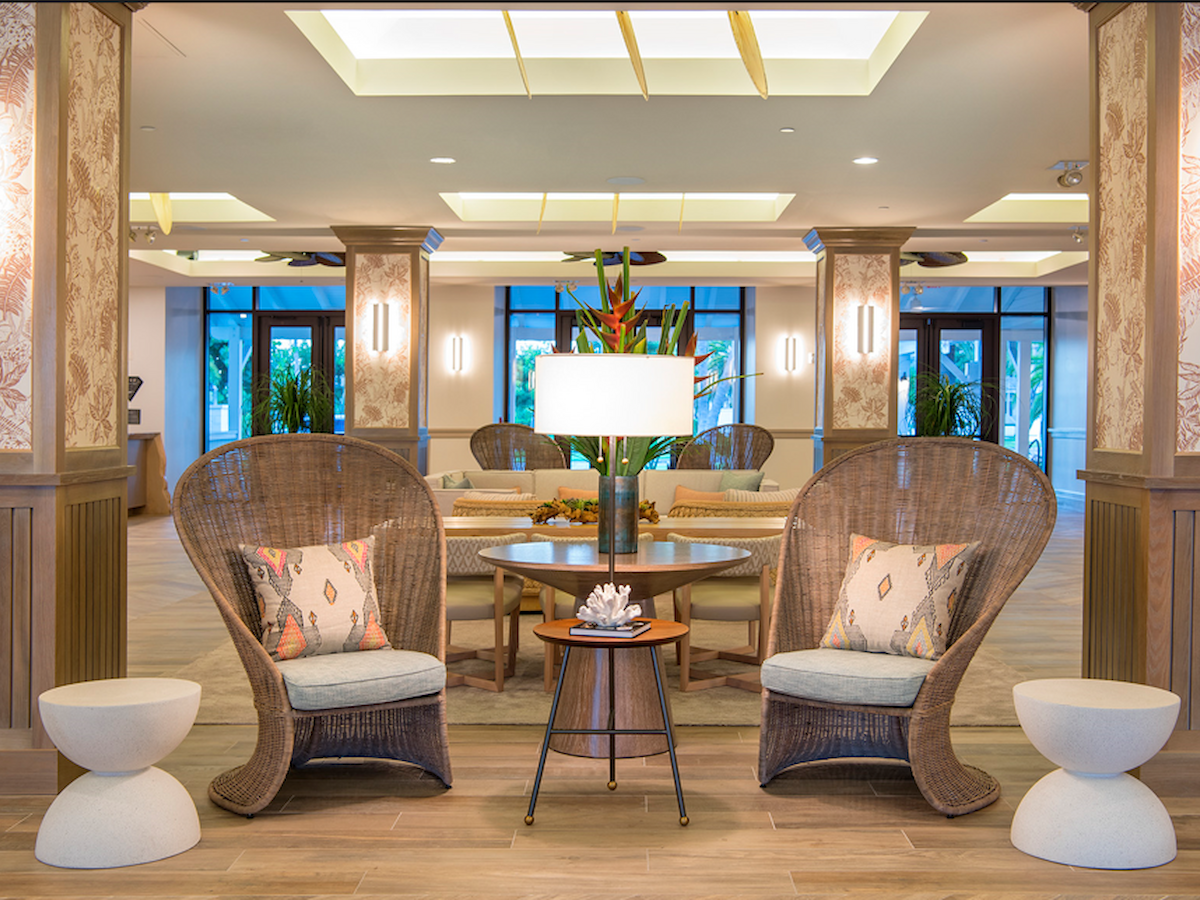 Cozy seating area in a stylish interior with wicker chairs, a lamp, and decorative plants. Bright windows and elegant lighting complement.